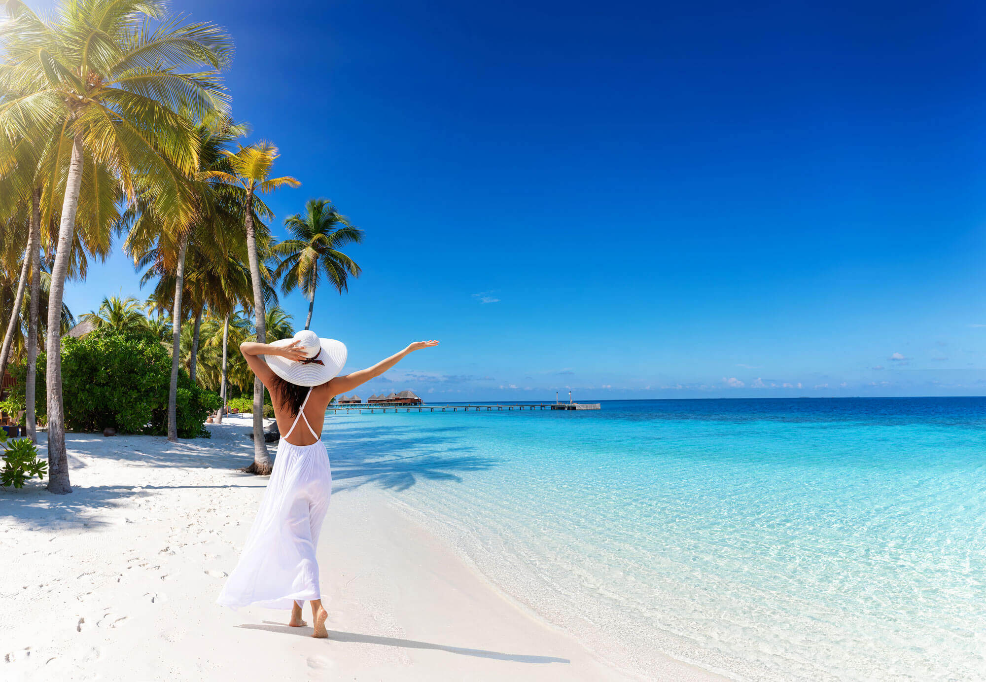 Malediven Urlaub-Frau im weißen Kleid am Strand neben dem türkisblauen Meer.