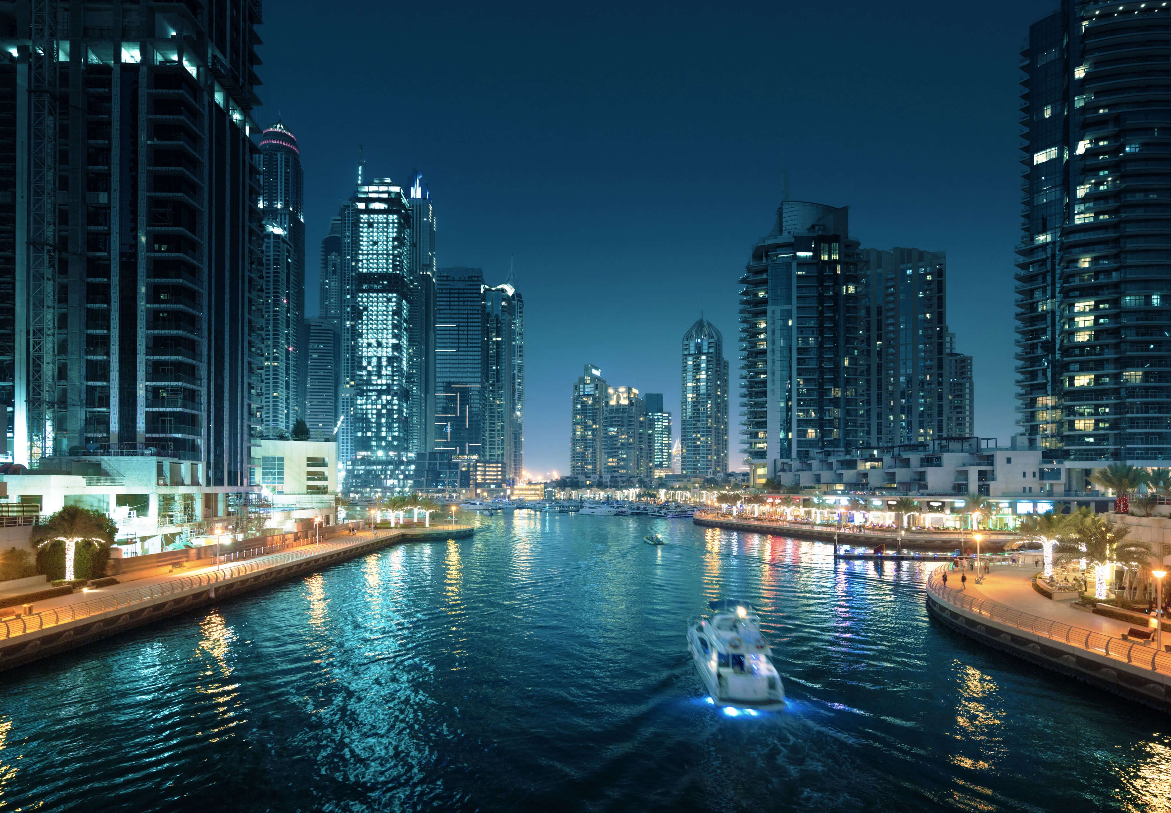 Dubai: Die Marina von Dubai bei Nacht mit einem Boot und hohen Gebäuden im Vordergrund