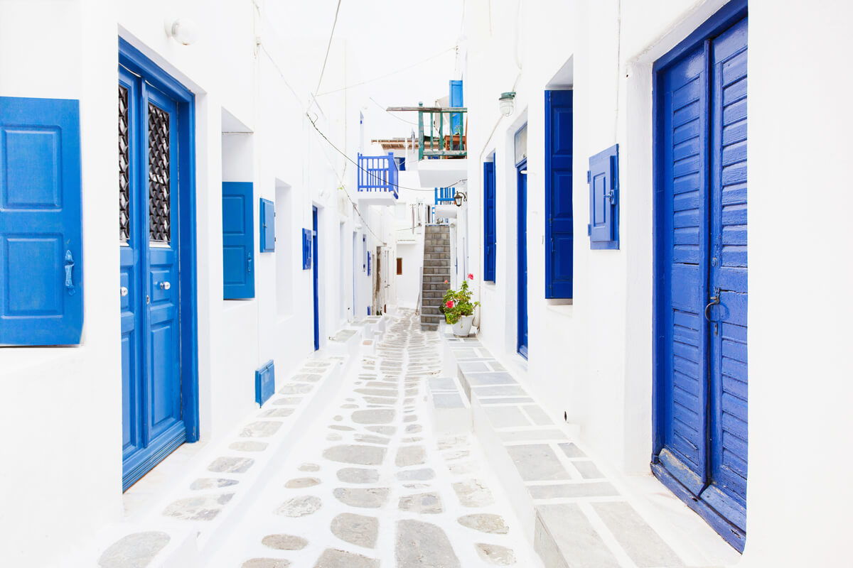 Gasse mit gepflastertem Weg, weißen Häusern und blauen Türen und Fenstern